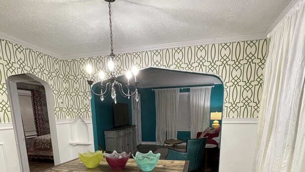Uma sala de jantar com mesa de madeira, tapete floral e papel de parede estampado.