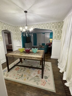 Un coin repas avec une table en bois, un tapis à motifs floraux et un papier peint à dessins.