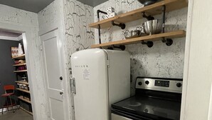 Uma cozinha compacta com geladeira branca, fogão e uma prateleira de madeira sobre o fogão.