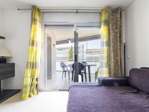 A bedroom with a bed, a desk, and a chair. There is a sliding glass door leading to a balcony with a table and chairs.