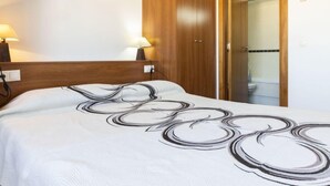 Ein Hotelzimmer mit einem Holzkopfteil, einem Bett mit einer weiß-schwarzen abstrakten Tagesdecke, zwei Nachttischlampen und einem Holzschrank.