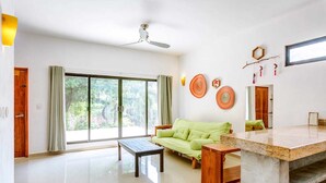 A spacious living room with a large sliding glass door leading to a garden, a ceiling fan, a green sofa, a wooden coffee table, and a marble countertop. - Stay in the heart of Tulum! footsteps away from the most vibrant street in town (Tulum)