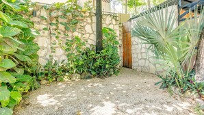 A stone wall with climbing plants, a palm tree, and a gravel path. - Stay in the heart of Tulum! footsteps away from the most vibrant street in town (Tulum)