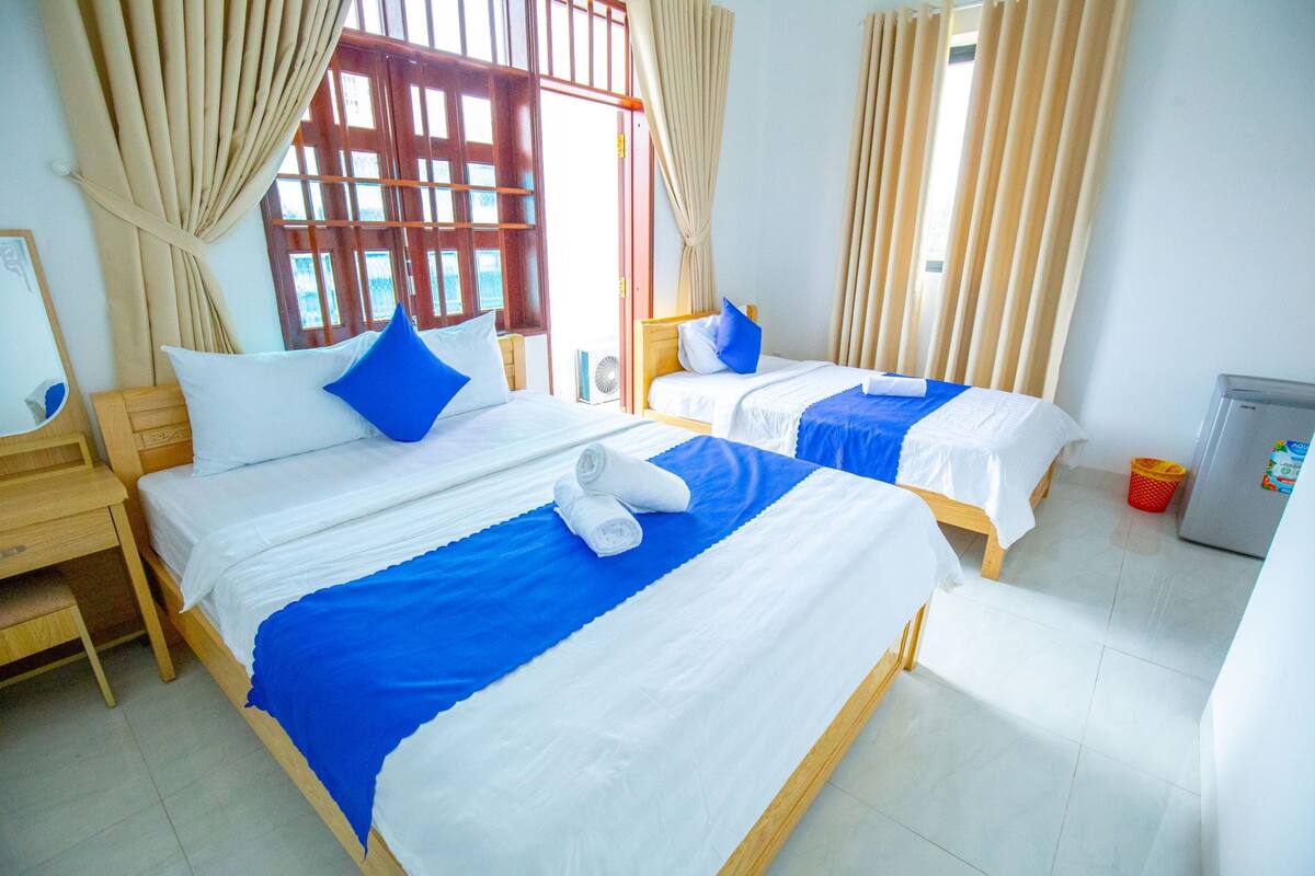 A hotel room with two beds, each with blue and white bedding, and a small refrigerator.