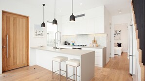 A modern kitchen with a central island, pendant lights, and a wooden door.