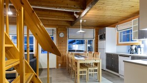 A modern kitchen with wooden flooring, a dining area with a wooden table and chairs, and a staircase with wooden railings. - Albatrossi by Interhome (Kittilä)