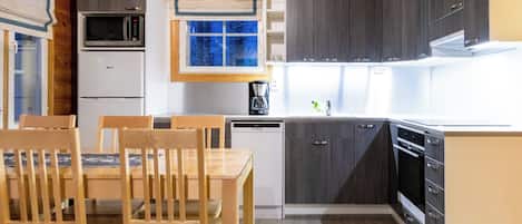 Een kleine keuken met houten kastjes, een magnetron, een koffiezetapparaat en een eethoek met houten stoelen en een tafel.