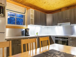 Een moderne keuken met houten kastjes, een inbouwoven en een eethoek met een tafel en stoelen.