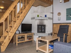 Una escalera de madera que lleva a una sala de estar con chimenea, televisor y una mesa.