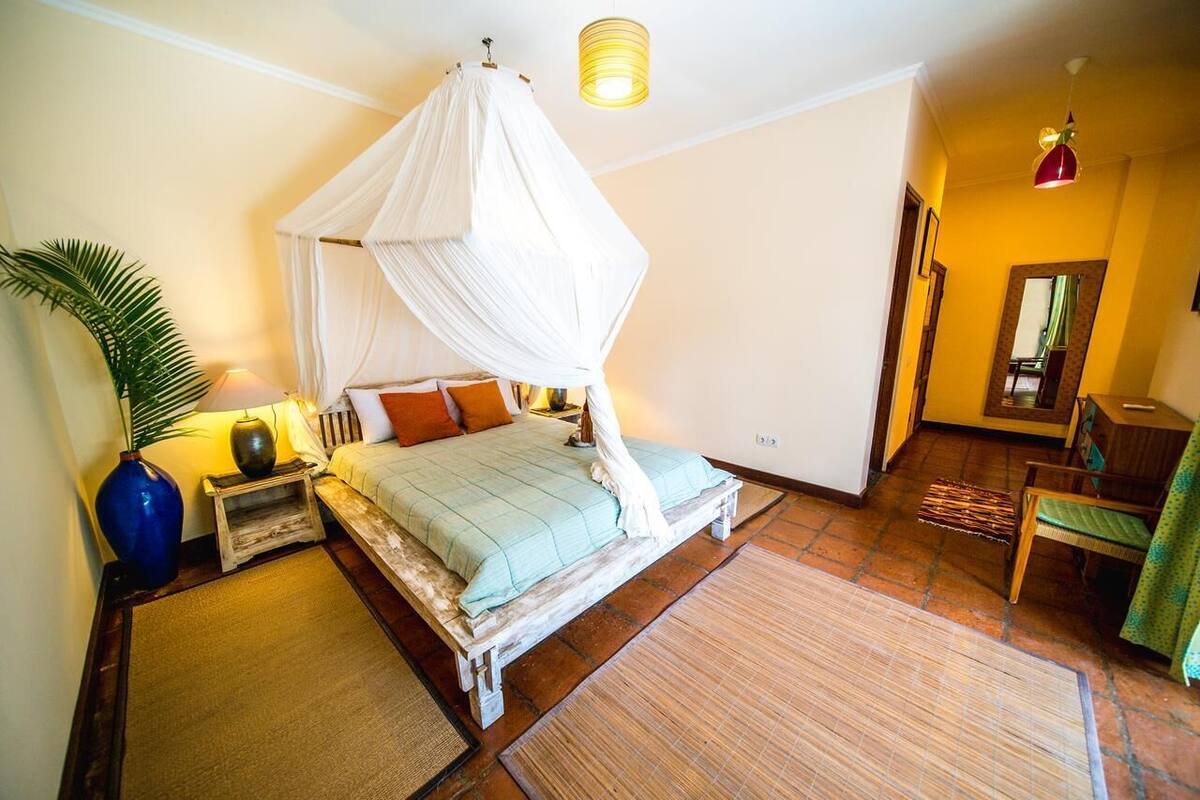 A bedroom with a canopy bed, a nightstand, a lamp, a chair, and a mirror.