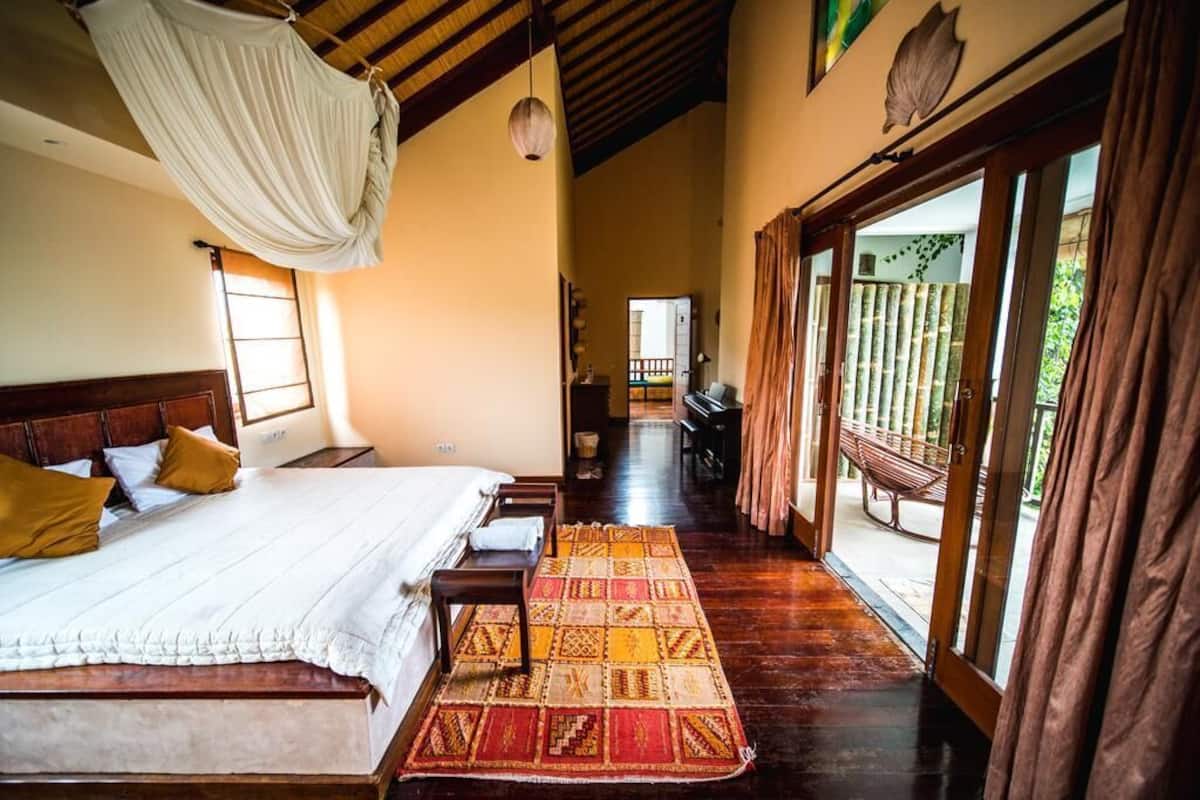A spacious bedroom with a large bed, a hanging canopy, and a view of the outdoors through a glass door.