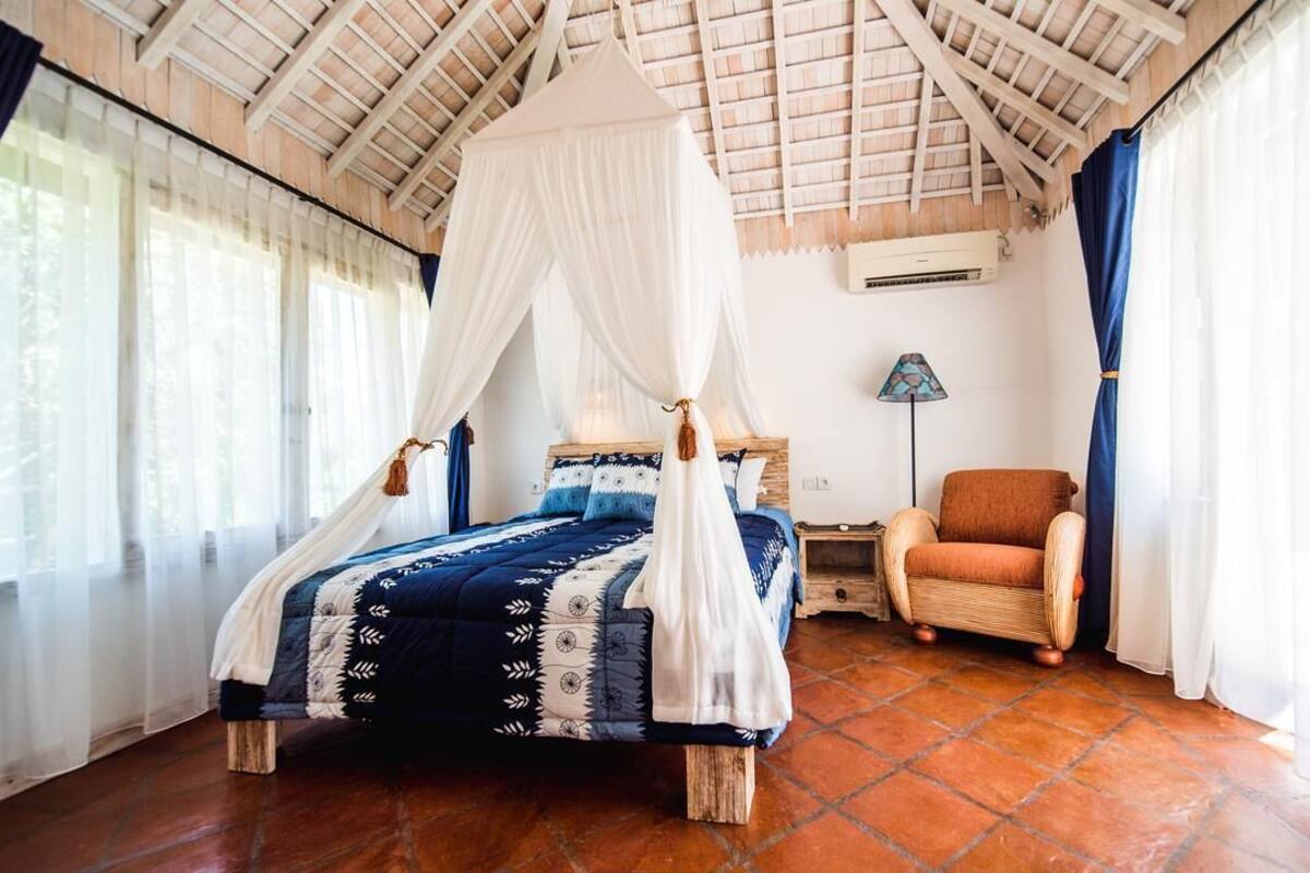 A bedroom with a four-poster bed, a wooden nightstand, a chair, and a lamp.