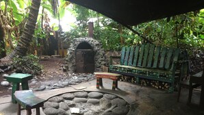 A rustic outdoor seating area with a stone fire pit, wooden benches, and a small table.