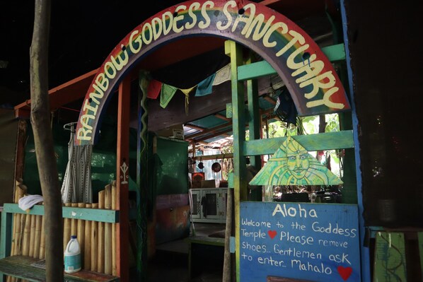 A colorful entrance to the Rainbow Goddess Sanctuary with a sign welcoming visitors and instructions to remove shoes.