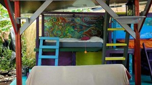 A colorful, enclosed sleeping area with a bunk bed, a ladder, and a hanging light fixture.