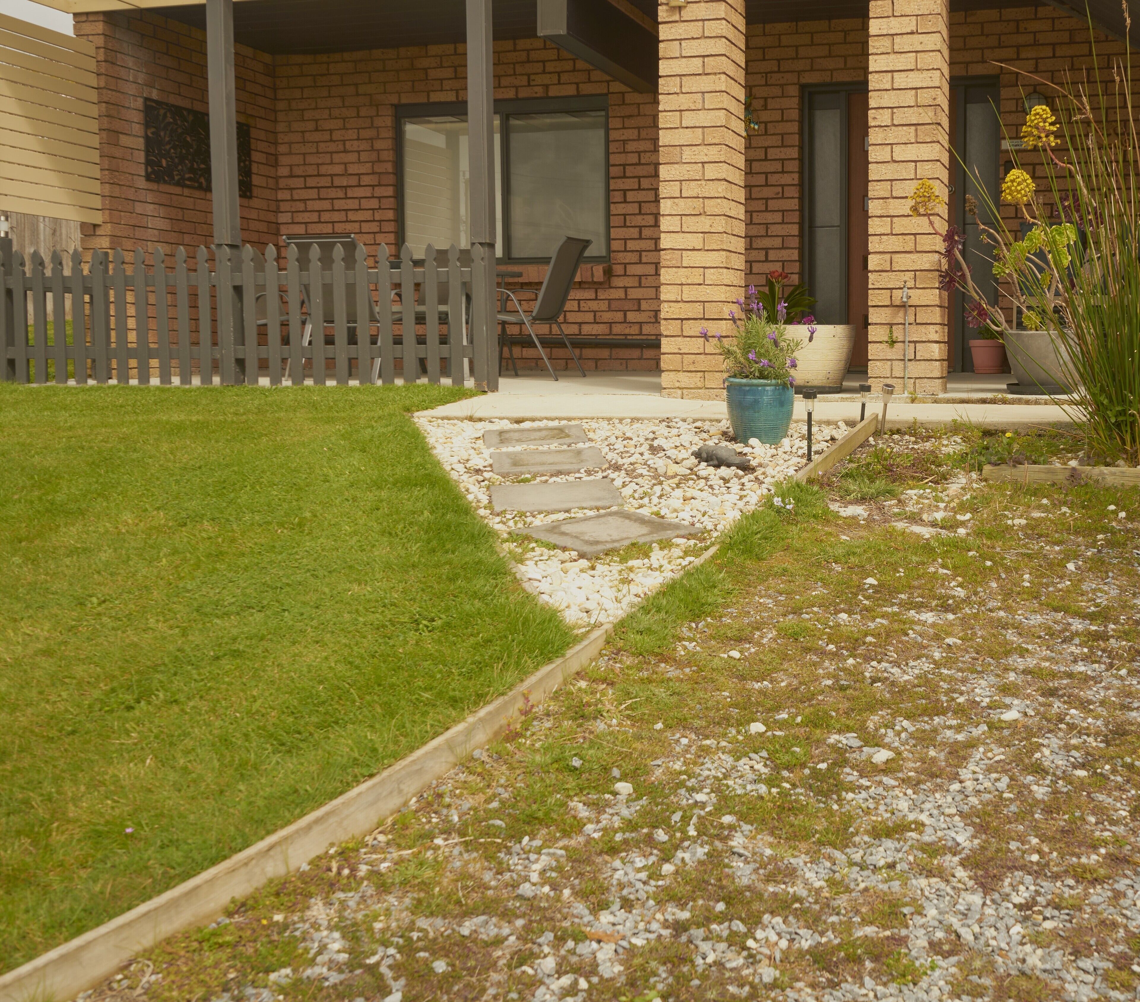 Una casa in mattoni con un recinto in legno bianco, un vialetto in pietra e un prato erboso.