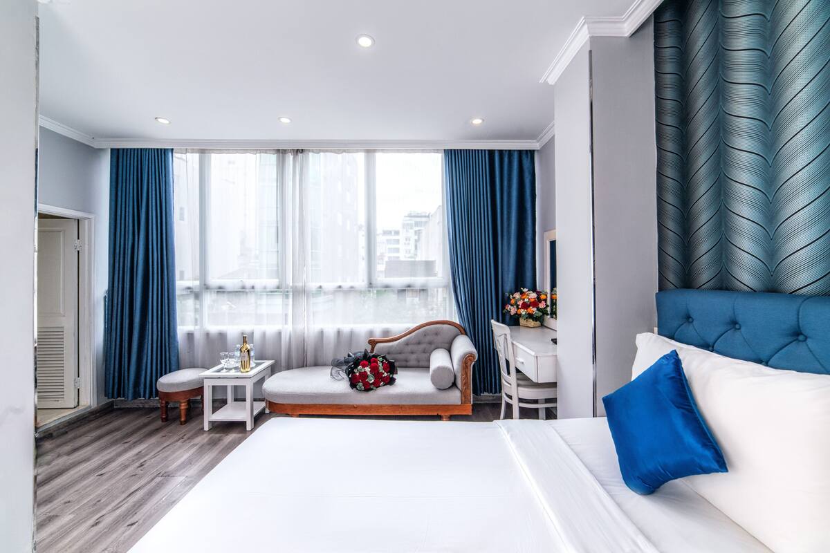 Une chambre d’hôtel moderne avec un grand lit, un canapé, une petite table agrémentée d’un bouquet de fleurs et un bureau avec une chaise.