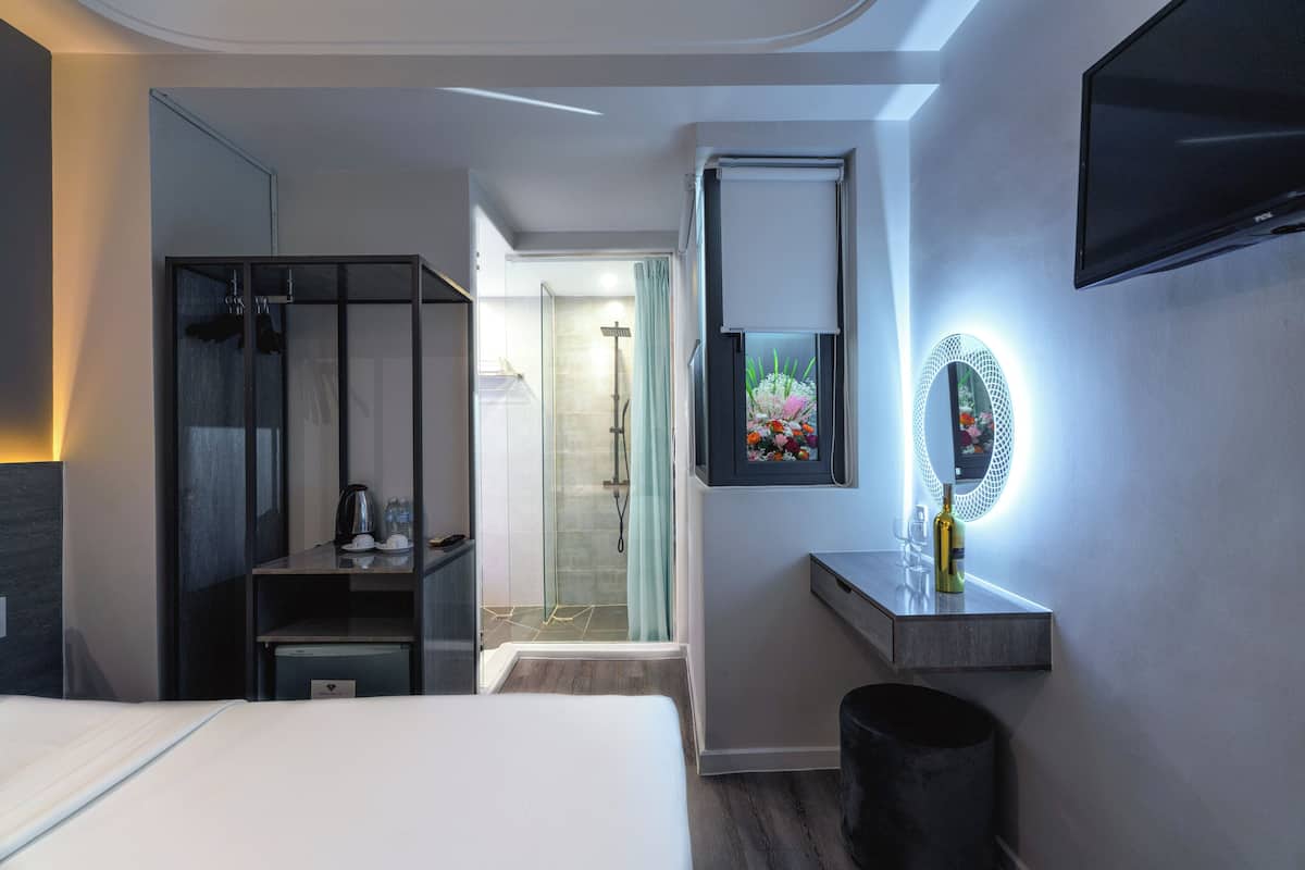 Une chambre d’hôtel moderne équipée d’un lit, d’une armoire, d’une coiffeuse avec un miroir et d’un téléviseur fixé au mur.