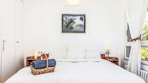 Un dormitorio ordenado con una cama grande, un cuadro en la pared y una ventana con cortinas.