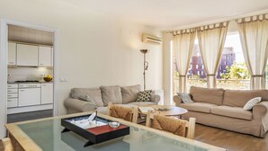 Una sala de estar moderna con una mesa de centro de vidrio, dos sofás, una mesa de comedor y una cocina con armarios blancos.