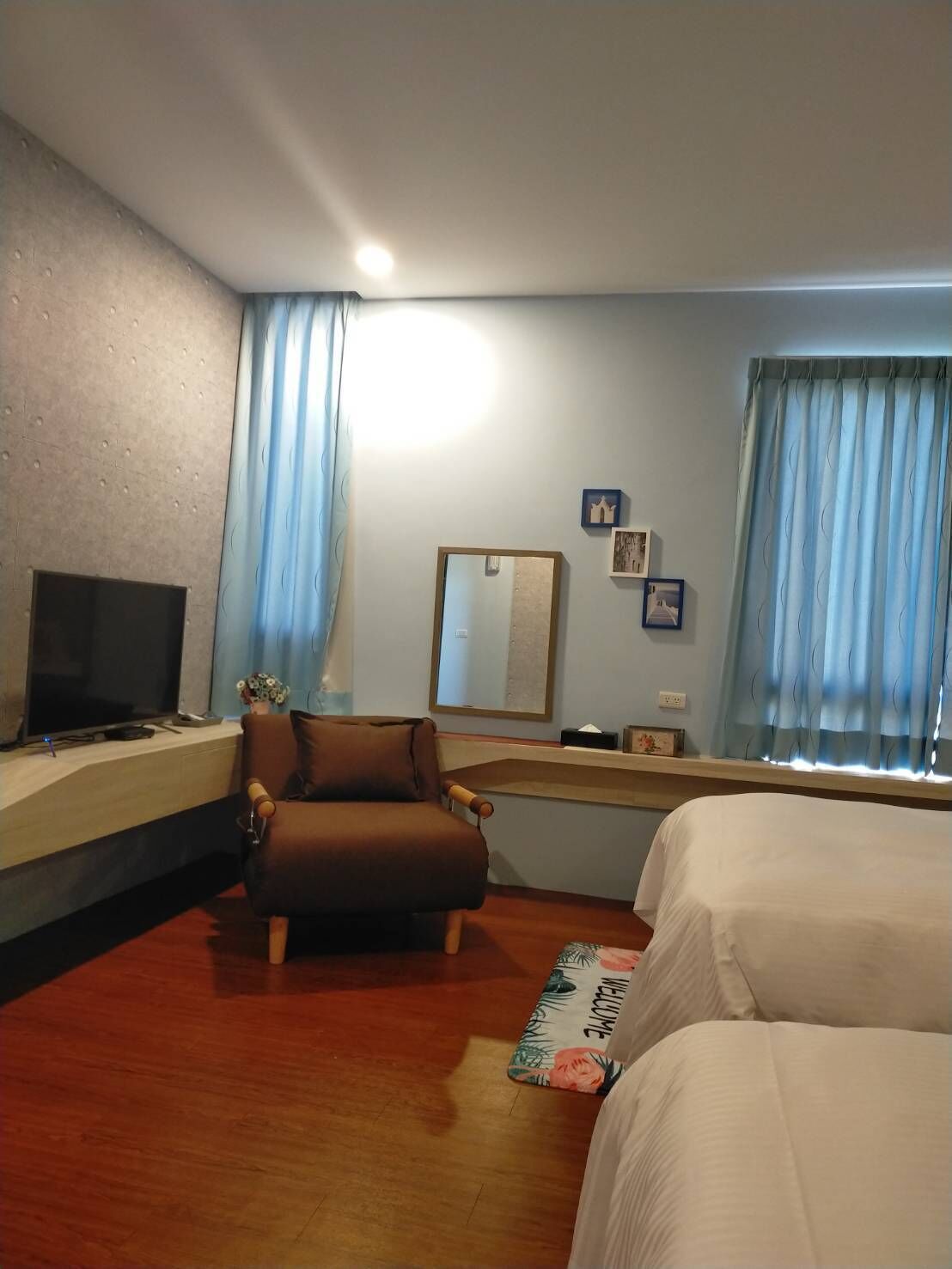 Habitación de hotel con cama, una silla, televisor, espejo y ventana con cortinas.