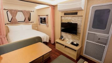 A compact bedroom with a bed, bedside table, TV, and a small seating area.