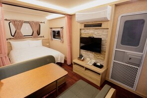 Una habitación pequeña con cama, mesita de noche, televisión y un rincón para sentarse.