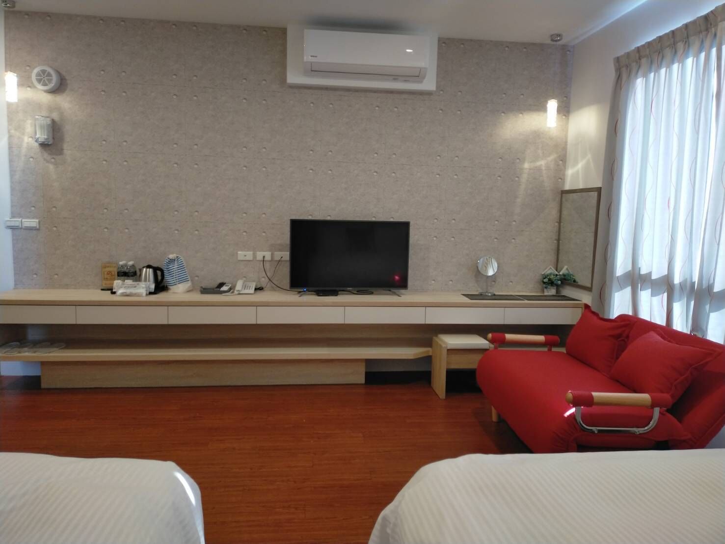 Ett hotellrum med en säng, en röd soffa, en tv och ett skrivbord med diverse föremål.