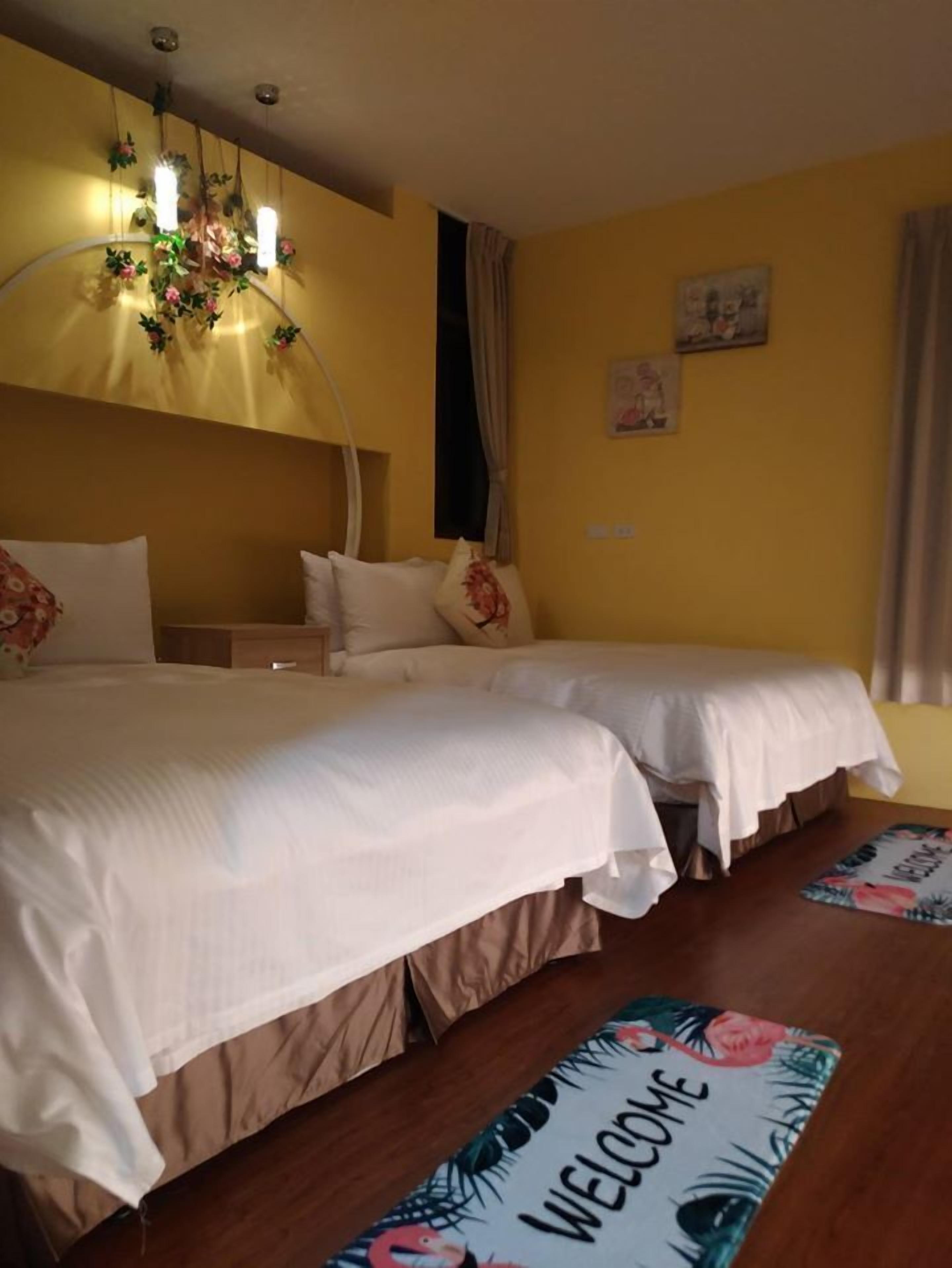 A hotel room with two beds, a chandelier, and a welcome mat.