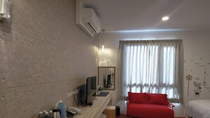 A modern hotel room with a wooden floor, a red sofa, a TV, and a window with curtains. - K-1 Hotel (Yuanlin)