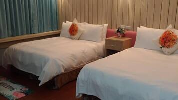 A hotel room with two beds, a wooden headboard, a nightstand, a wall-mounted lamp, and a window with curtains.