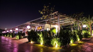 A covered outdoor area with a row of small trees and lights, a building with a sign, and a pathway. - K-1 Hotel (Yuanlin)
