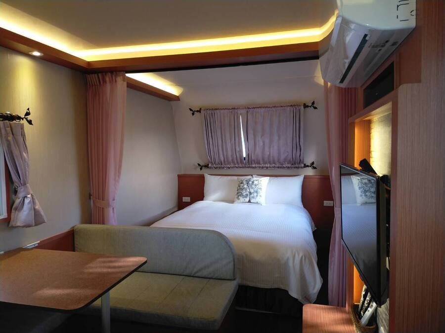 A hotel room with a bed, a small table, a sofa, a TV, and an air conditioning unit.