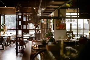 Un restaurante con mobiliario de madera, plantas colgantes y un amplio ventanal.
