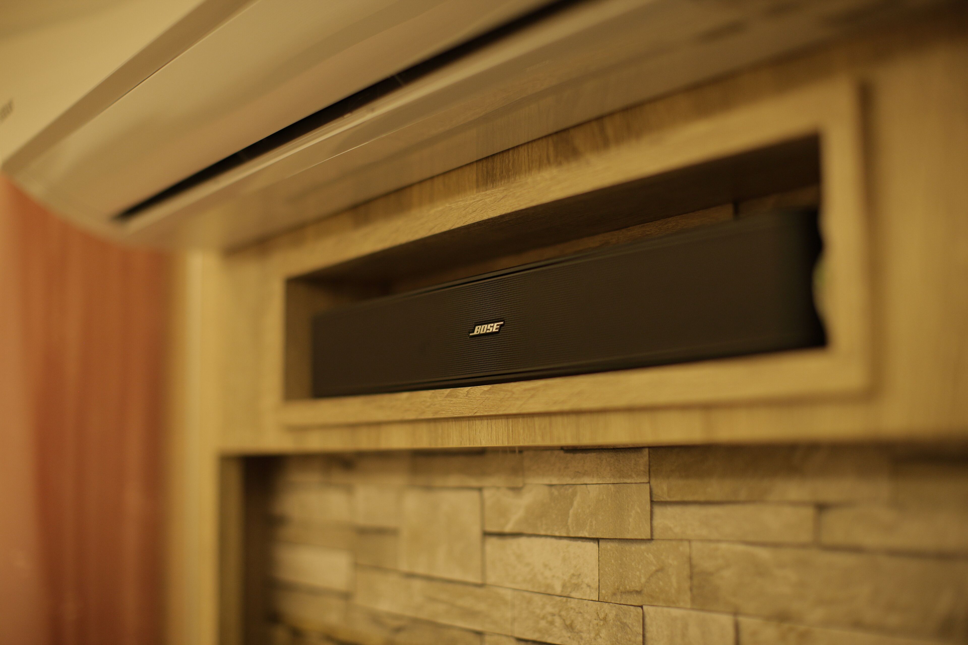 A wall-mounted air conditioning unit with a wooden panel and stone-like texture below it.