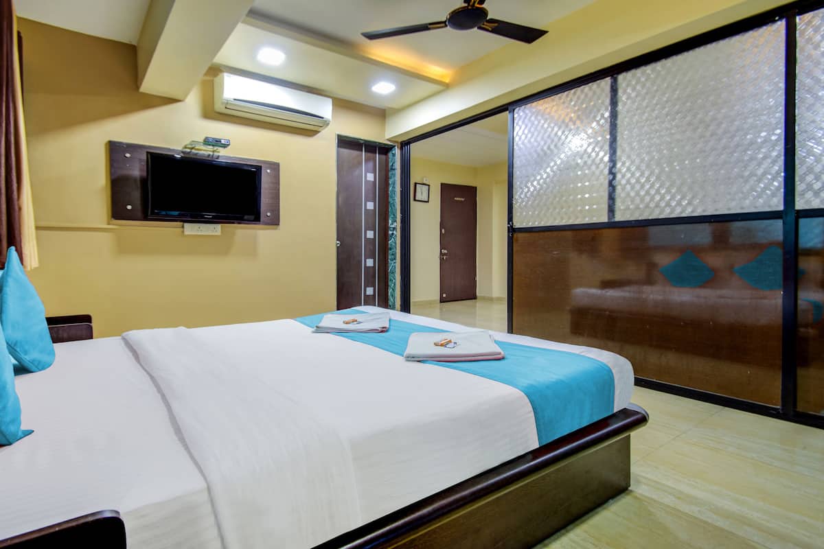 A hotel room with a bed, a flat-screen TV mounted on the wall, an air conditioning unit, and a sliding door leading to a balcony.