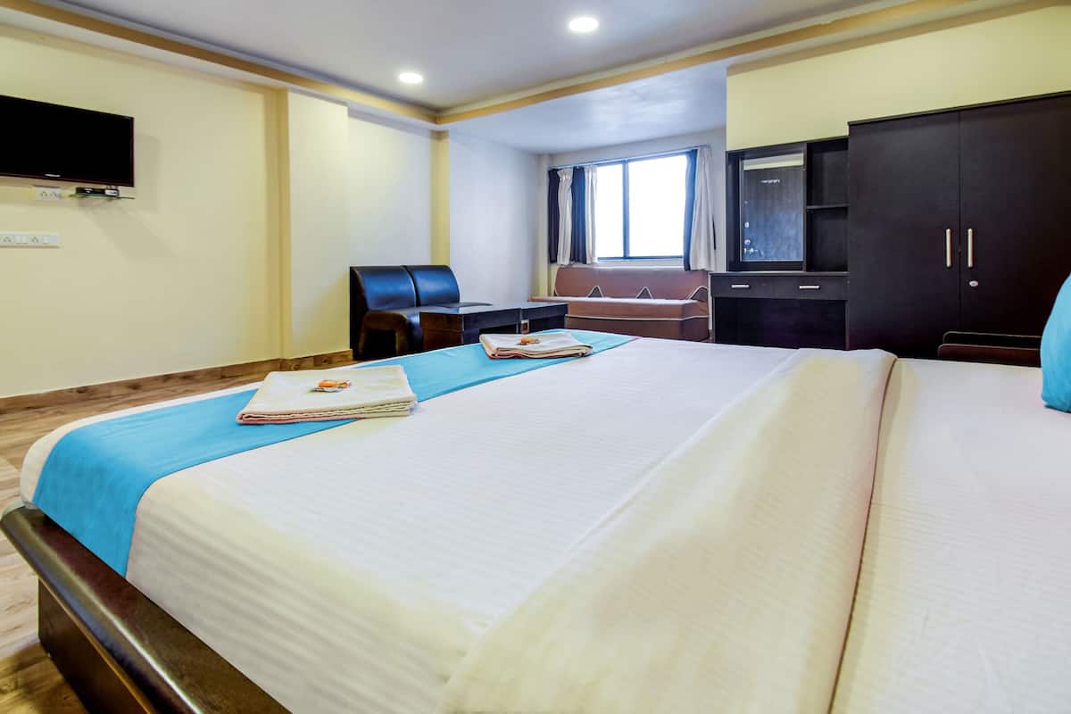 A hotel room with a large bed, a desk, a chair, a wardrobe, and a television on the wall.