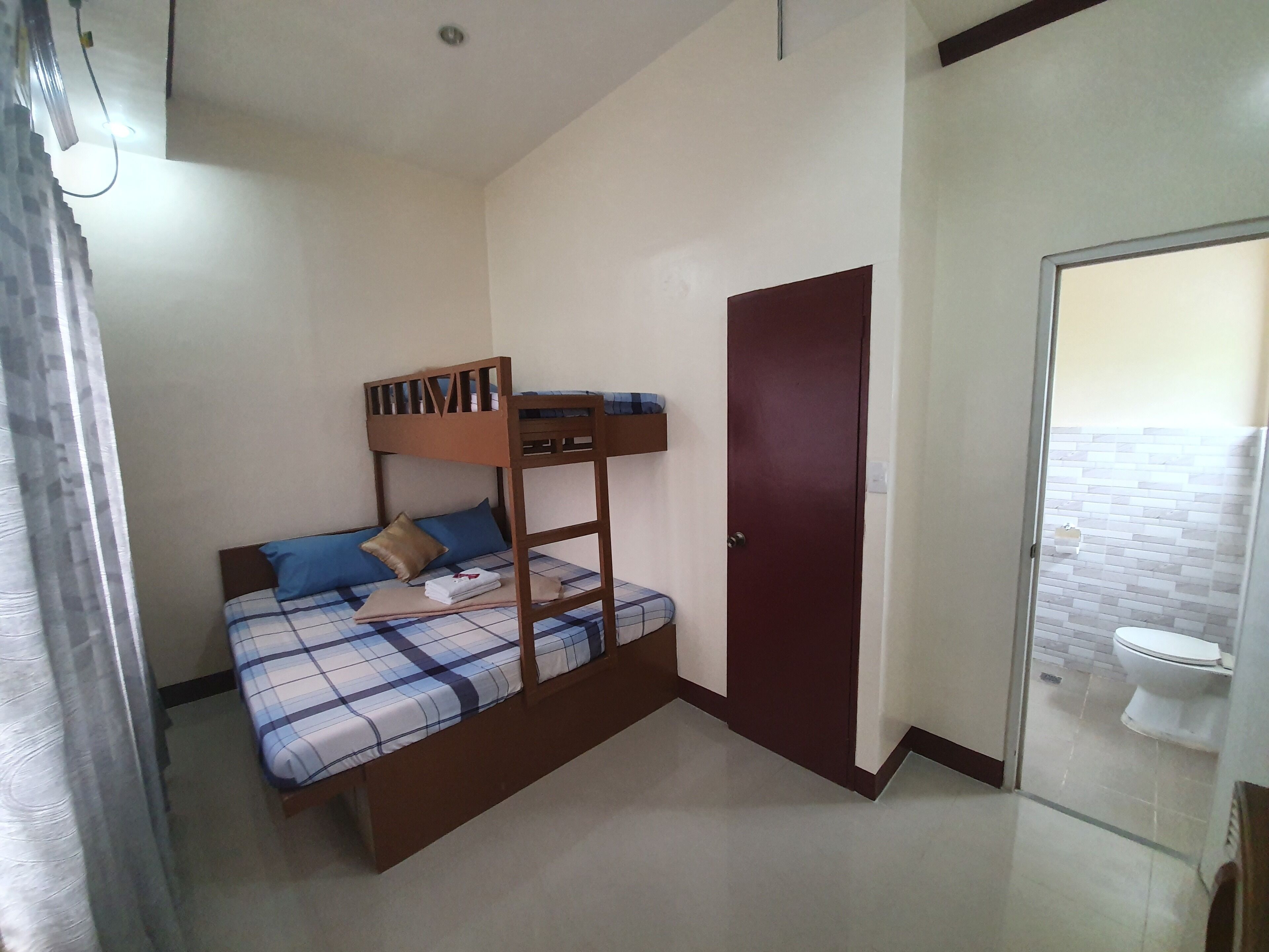 A small, simple room with a bunk bed, a door, and a bathroom visible through a glass partition.