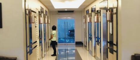 A hotel corridor with a checkered floor, a person walking, and a view of the sky through the ceiling.