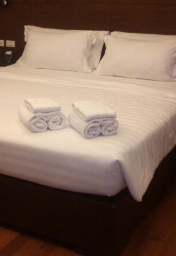 Un lit bien fait, avec du linge de lit blanc et deux serviettes enroulées posées sur le lit.