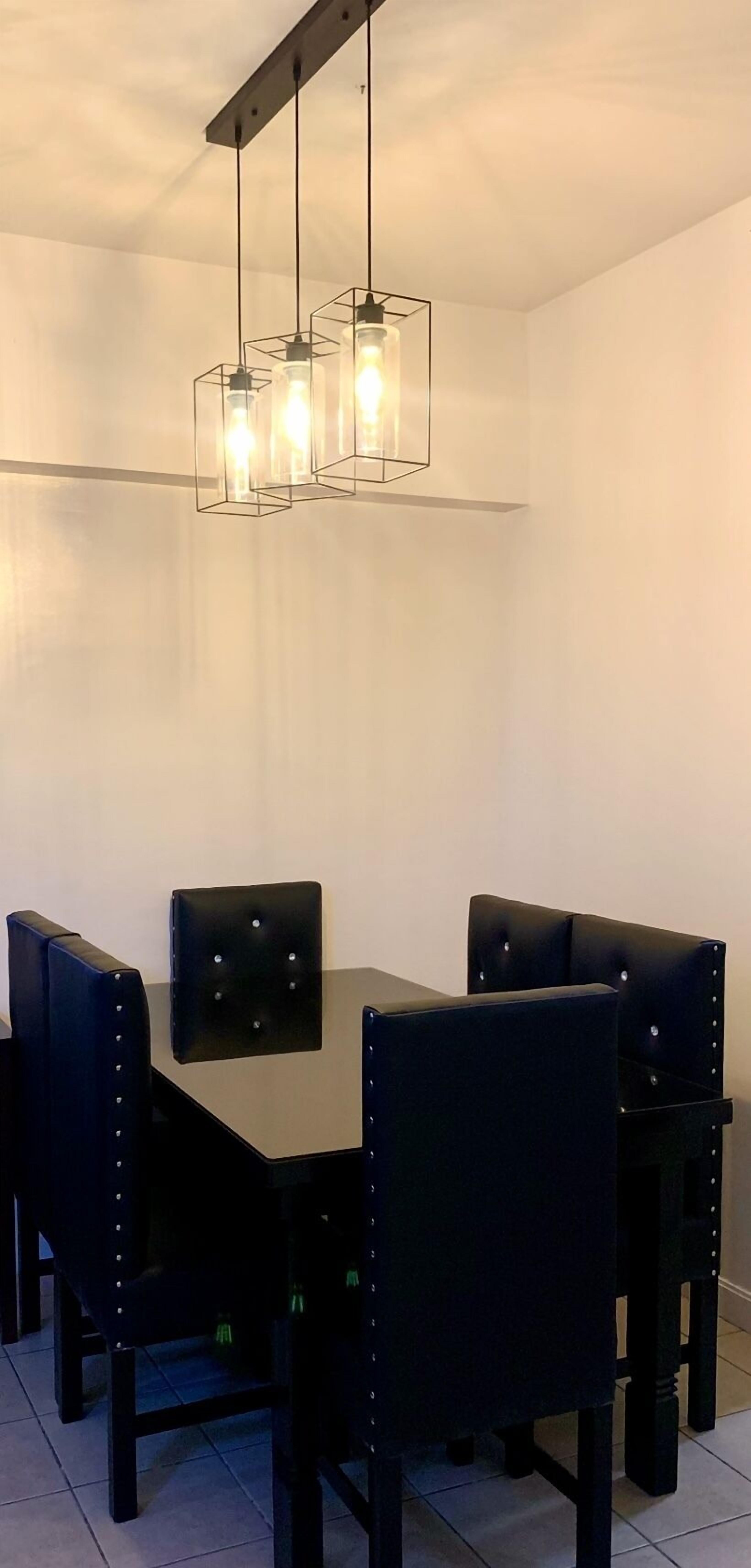 A dining area with a rectangular table and four upholstered chairs with metal studs. Three pendant lights hang from the ceiling above the table.
