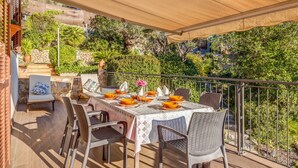 A dining area with a table set for four, surrounded by wicker chairs, a covered patio, and a view of a lush garden. - Beautiful Holiday Home Miravall with Mountain View (Puigpunyent)