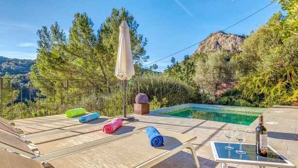 A poolside area with lounge chairs, a table with glasses and a bottle, and a view of a mountain. - Beautiful Holiday Home Miravall with Mountain View (Puigpunyent)