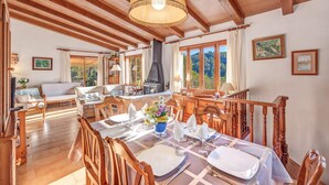 A dining area with wooden furniture, a central table set for a meal, and a large window overlooking greenery. - Beautiful Holiday Home Miravall with Mountain View (Puigpunyent)