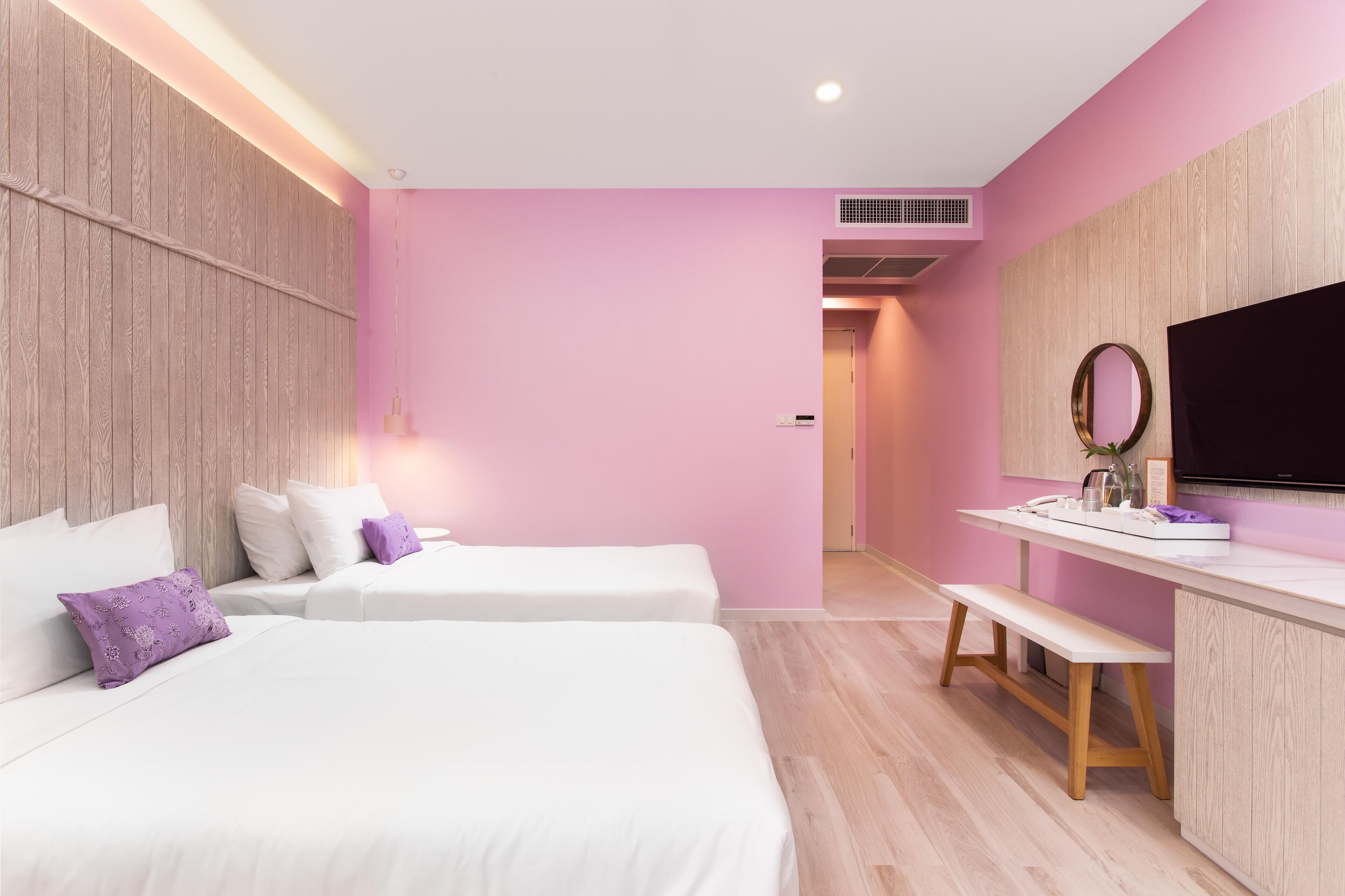 A hotel room with two beds, a desk, a TV, and a mirror.