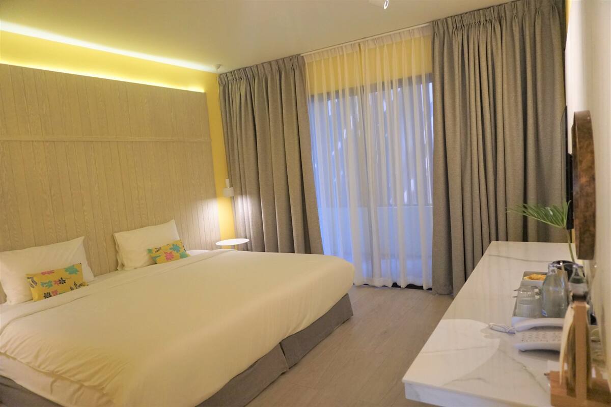 Una habitación de hotel con una cama grande, un escritorio con teléfono y una ventana con cortinas.