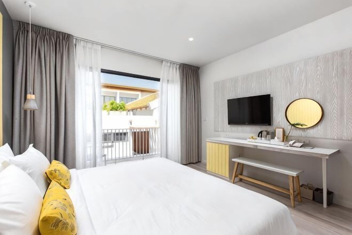 Una habitación de hotel moderna con una cama grande, un escritorio con televisor de pantalla plana y un balcón con vistas.