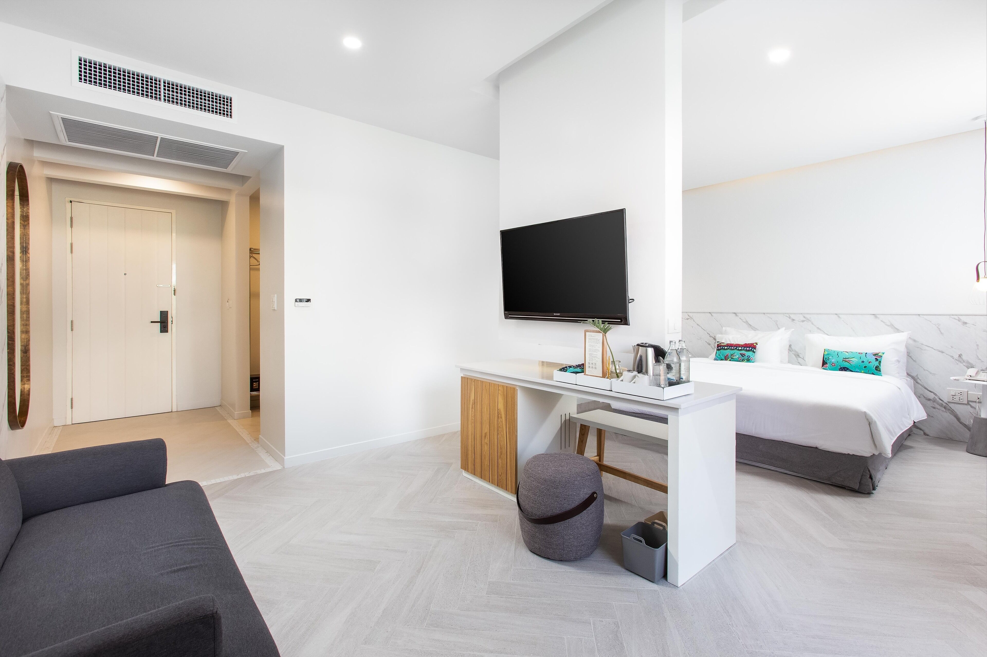 Une chambre d’hôtel moderne équipée d’un lit, d’un bureau avec un téléviseur à écran plat, d’un canapé et d’un petit pouf.