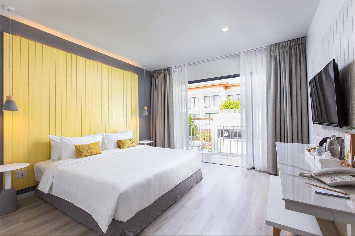 A modern hotel room with a large bed, a desk with a telephone, and a TV.