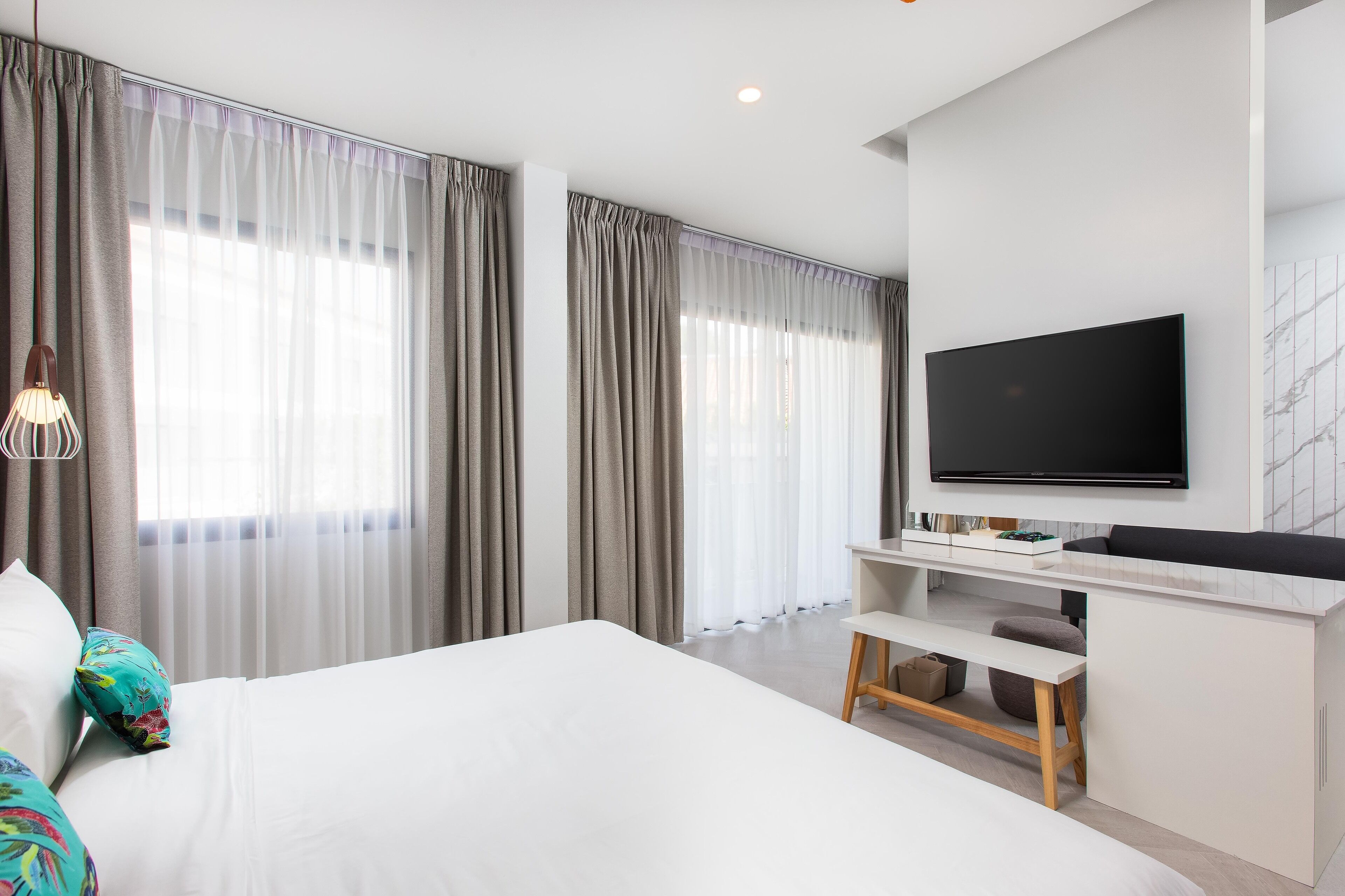 A modern hotel room with a large bed, a desk with a flat-screen TV, and a large window with curtains.